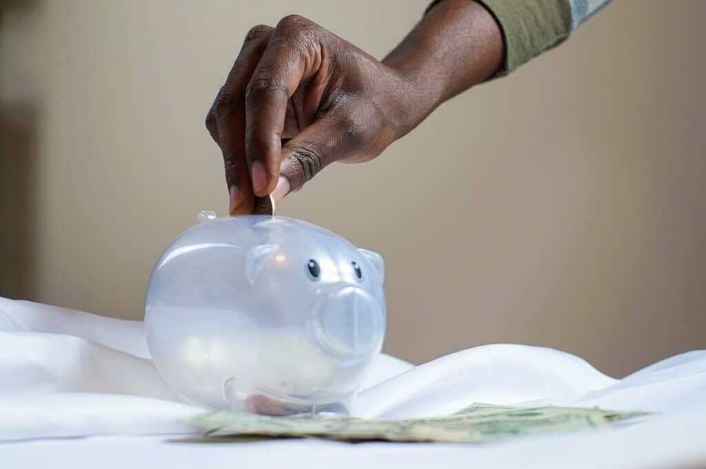 Black hand putting a coin into a clear piggy bank