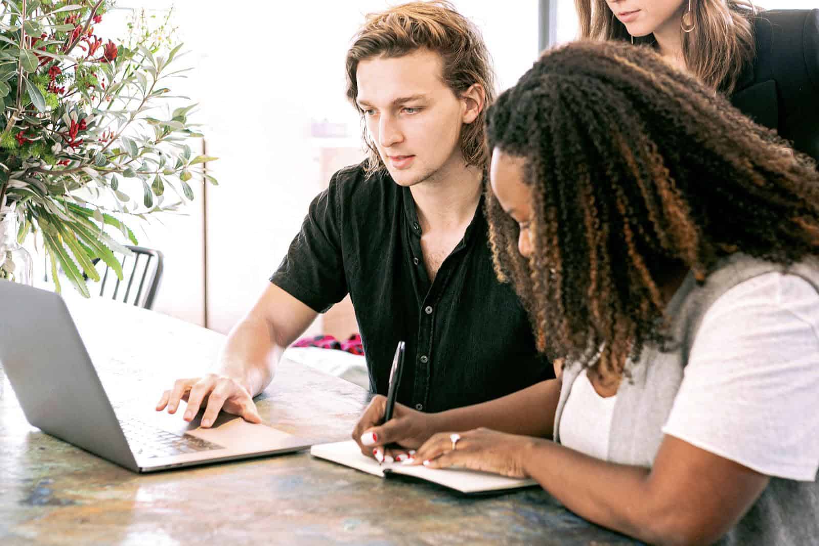 A boy pressing a laptop and a girl taking notes