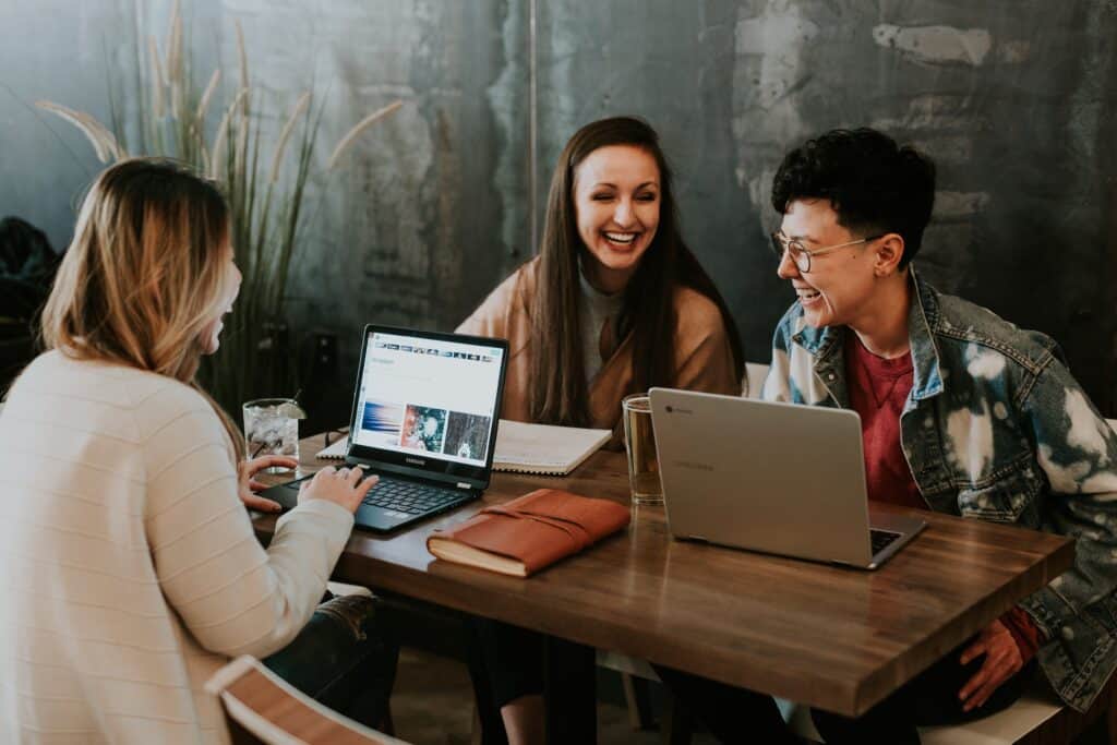 Young adults laughing over computers in cafe