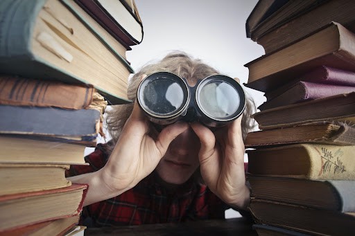 Man-between-stacks-of-books-looks-through-binoculars