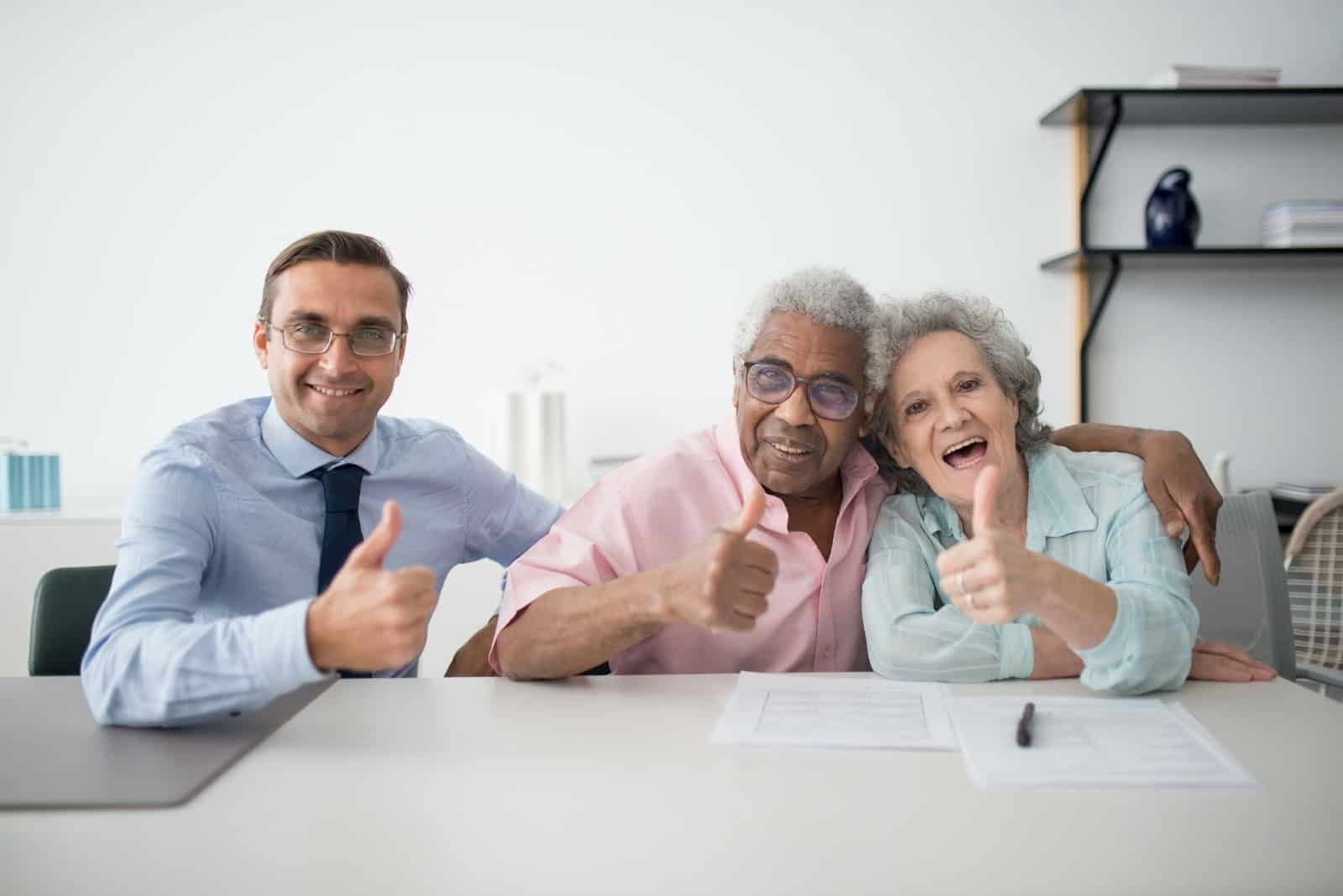 Business owner sitting with two elderly happy customers giving thumbs up.