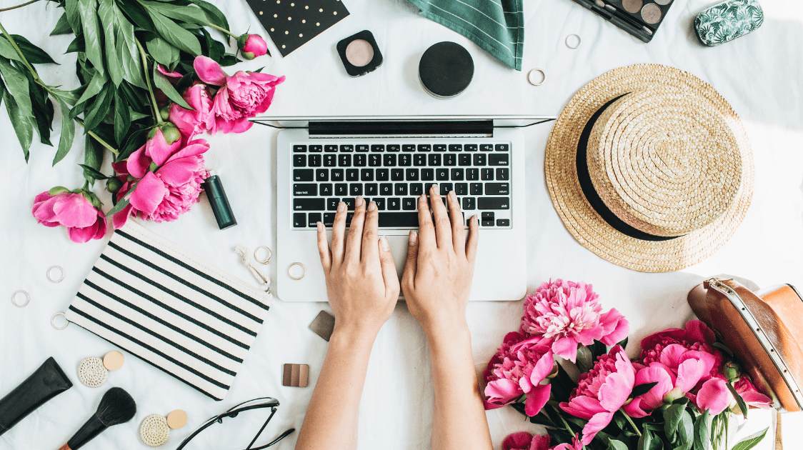 Woman's hands typing on a laptop keyboard surrounded by various items on the table