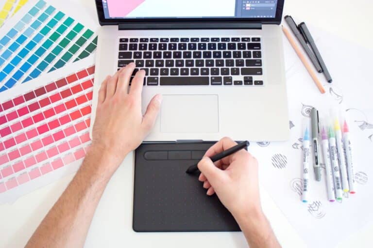 A graphic designer at work on his laptop with a pen input and color swatches